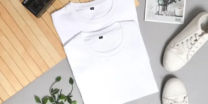 Two folded white t-shirts neatly arranged with white sneakers and a vintage camera.