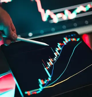 A hand points a stylus at financial graphs on a digital tablet screen.