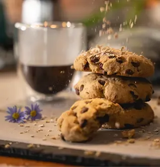Homemade chocolate chip cookies stacked, with sprinkles falling and a drink in the background.