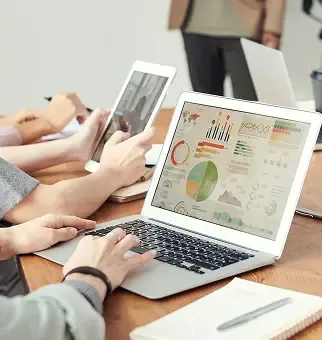 People collaborate around a table, viewing charts on a laptop and a tablet.