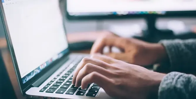 Close-up of hands typing on a laptop keyboard with a white screen visible.