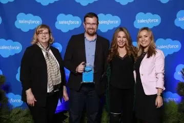 Four people, two men and two women, pose with a Salesforce award on stage.