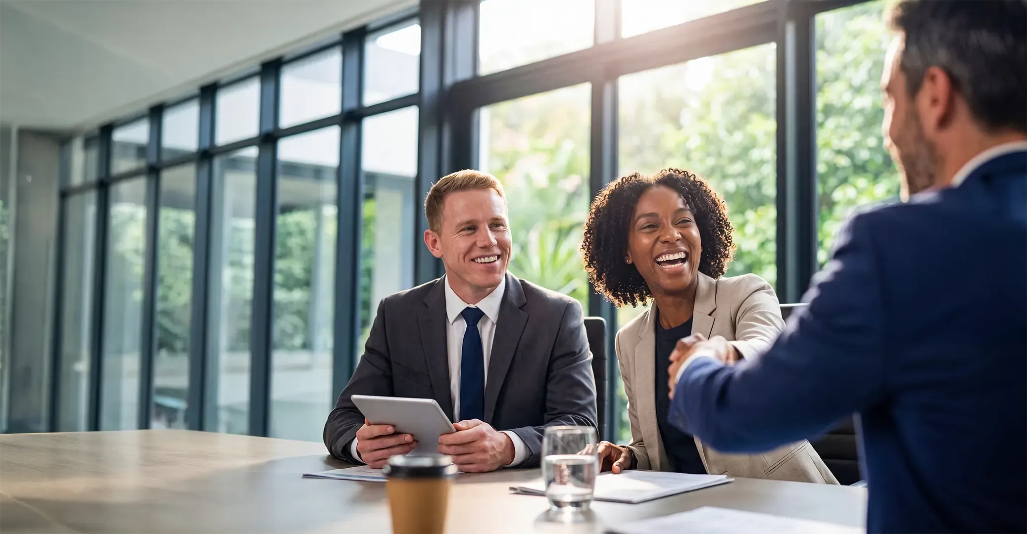 Diverse professionals smiling, shaking hands in a bright, modern office during a business meeting.