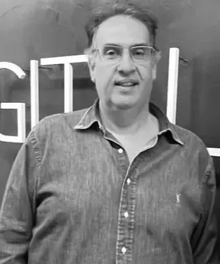 Black and white portrait of a man with glasses wearing a denim shirt.