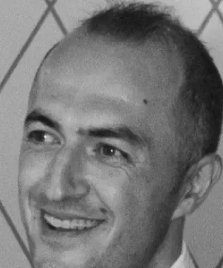 Black and white close-up of a smiling bald man looking to the side.