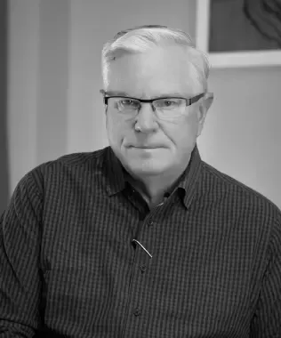 Black and white headshot of a man with grey hair, glasses, and a serious expression.