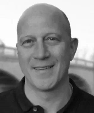 Black and white headshot of a smiling bald man outdoors.
