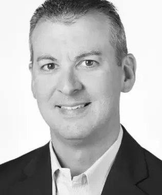Black and white portrait of a smiling man with a beard, wearing a casual shirt.