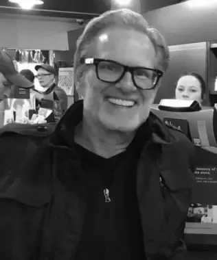 Black and white headshot of a smiling man with glasses, a beard, and a jacket.