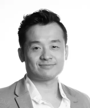 Black and white portrait of a man with glasses, beard, and a QR code pin.