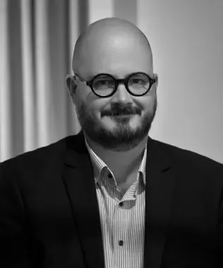 Black and white portrait of a smiling man in a puffer vest.