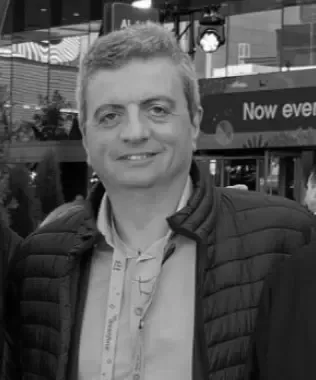 Black and white portrait of a smiling woman with curly blonde hair and glasses.