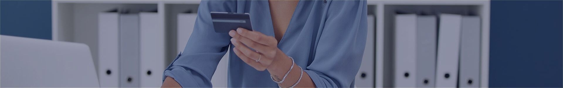 A person in a blue shirt holds a smartphone in an office environment.