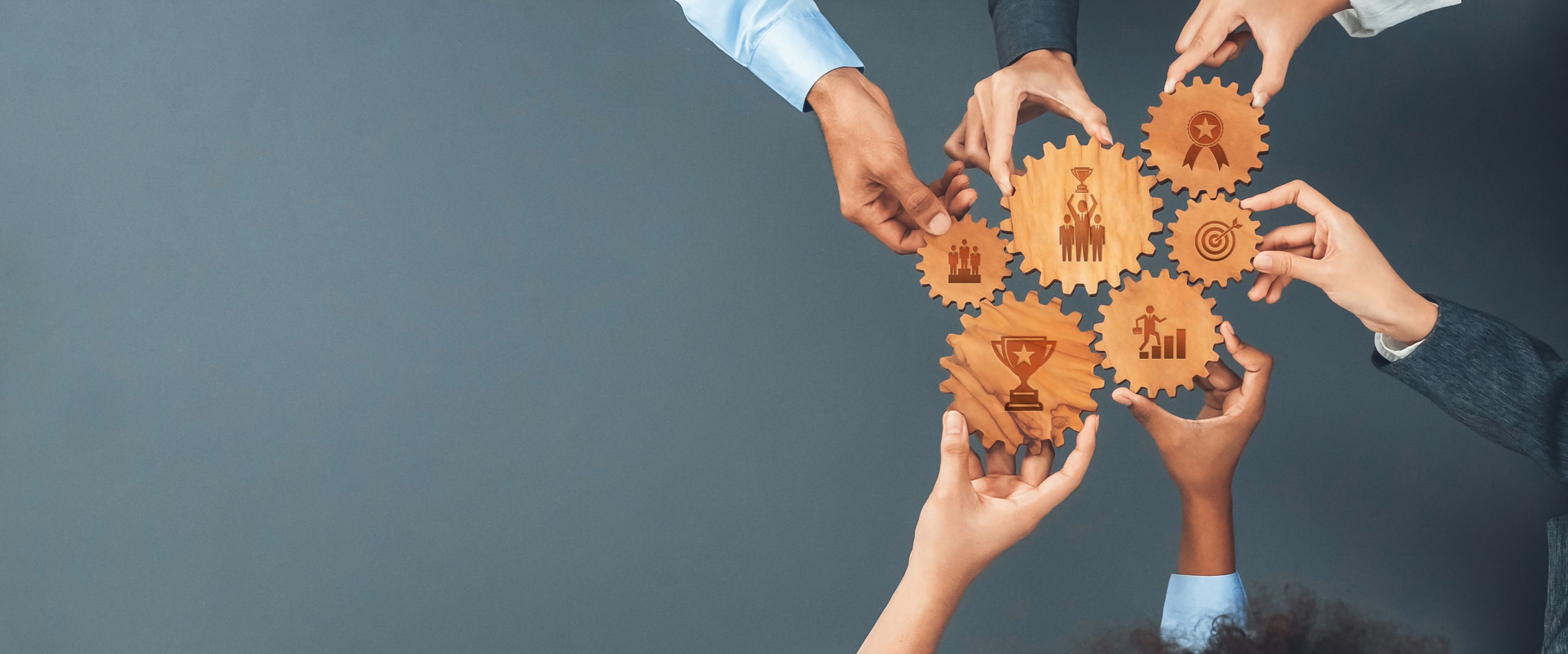 Hands connecting wooden gears with various business icons, symbolizing teamwork and a collaborative system.
