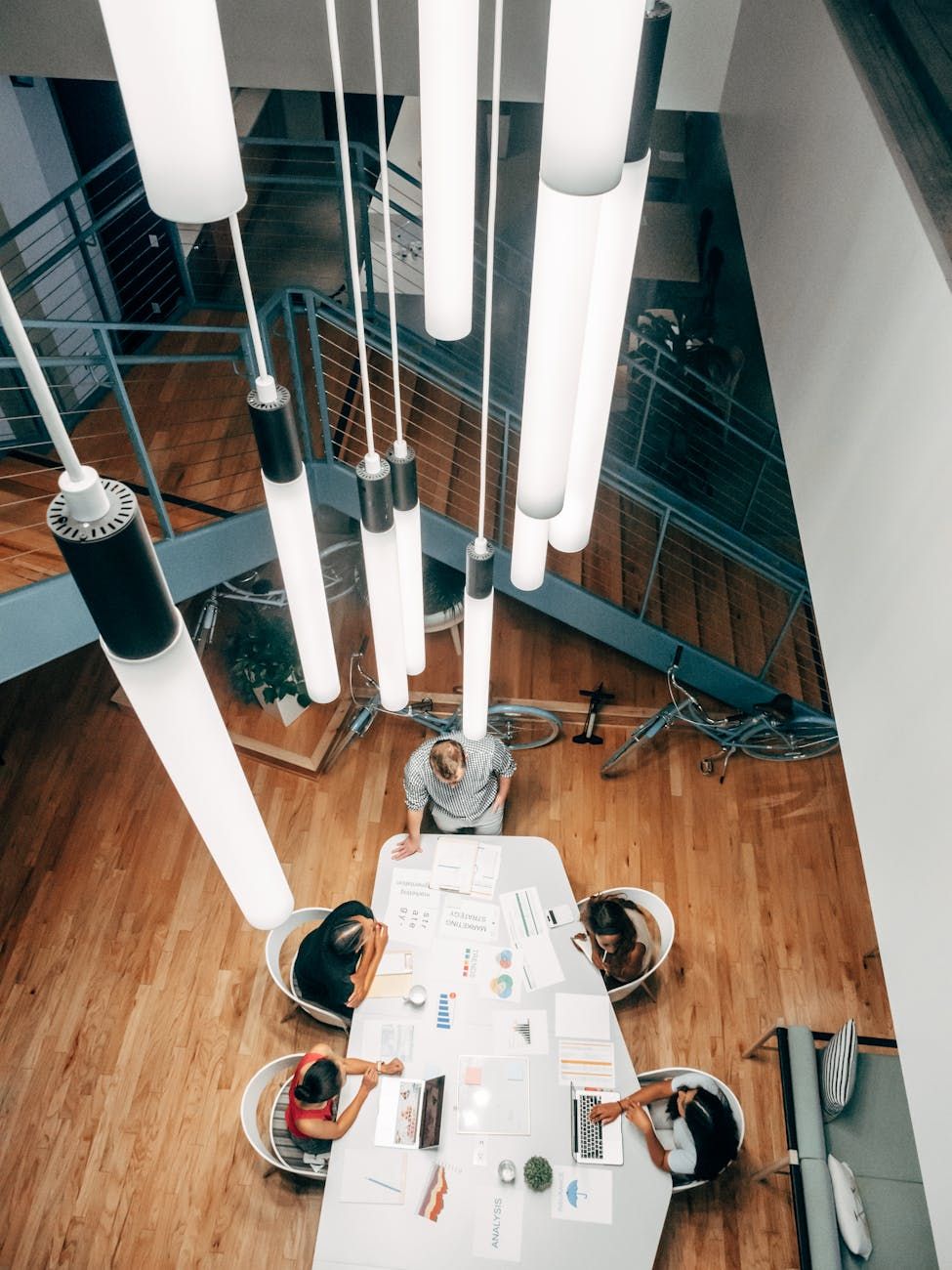 Overhead view of a modern dining table with place settings under tall pendant lights.