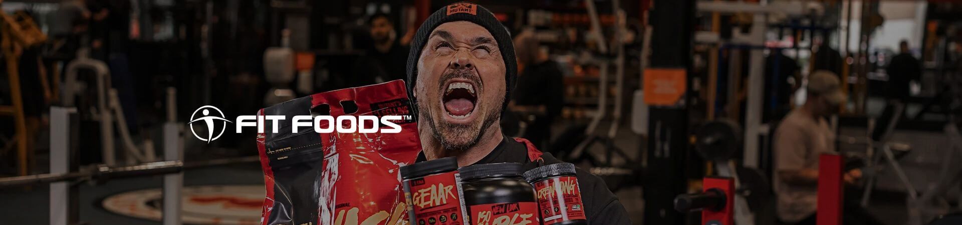 Excited man in a red jacket shouts in a gym with the Fit Foods logo.