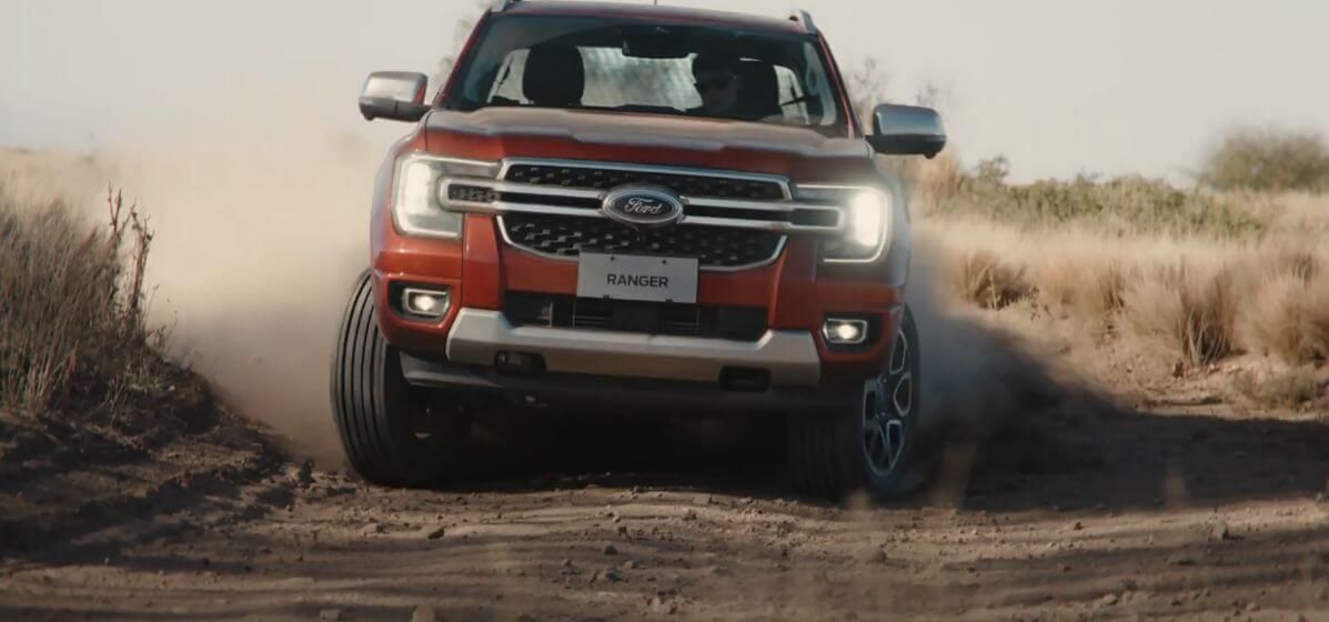 Red Ford SUV driving on a dusty dirt road, kicking up dirt as it moves.