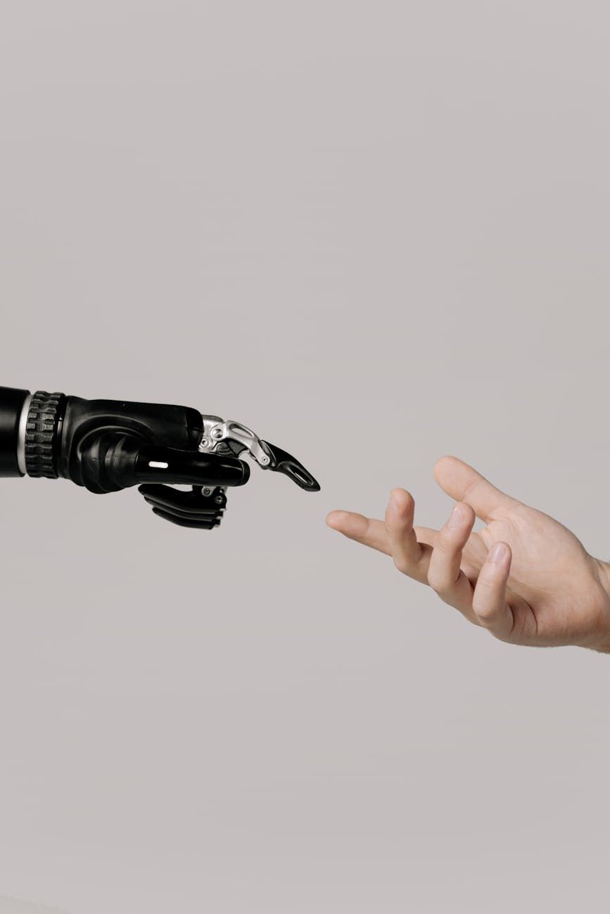 A black robotic hand and a human hand with index fingers nearly touching.
