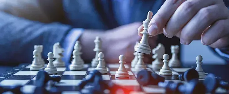 Hand moving a white king chess piece on a chessboard, strategic game planning.