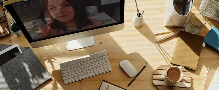 Overhead view of a modern desk with computer, keyboard, coffee cup, and video call.