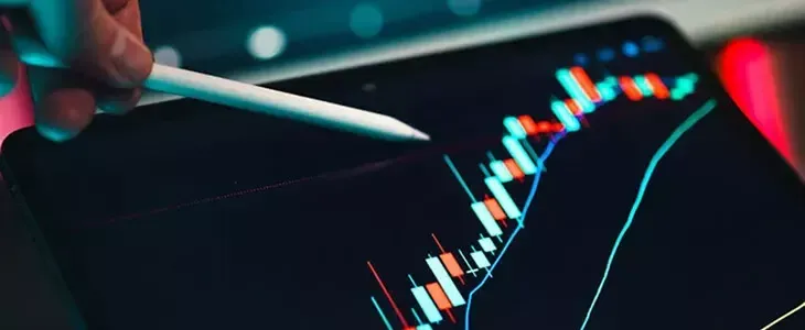 Hand with stylus pointing at financial graphs and data on a digital tablet screen.