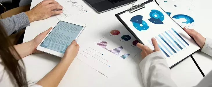 Two people analyzing business charts, graphs, and data on a tablet and clipboard.