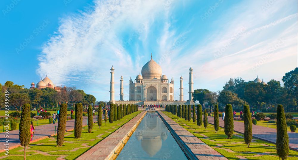 Taj Mahal mausoleum with its reflection in a long pool, surrounded by green gardens.