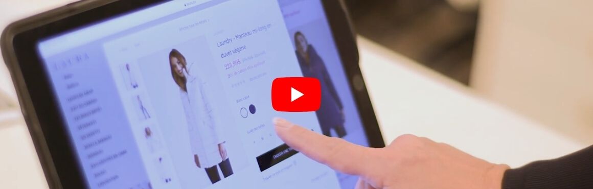 Finger interacting with a tablet displaying an e-commerce clothing page and play button.