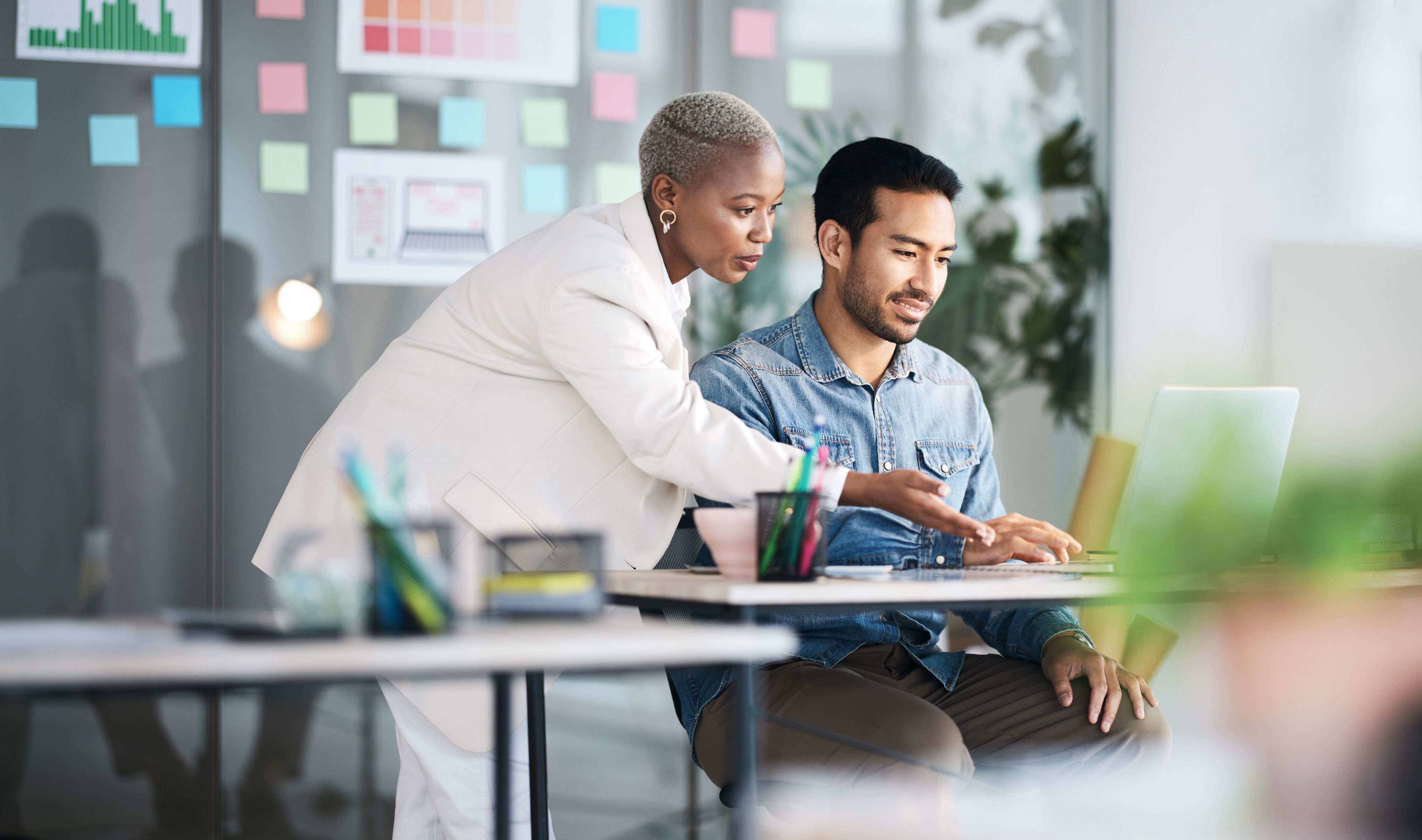 Two colleagues, a woman and a man, collaborate on a laptop in a modern office.