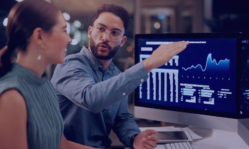 Two professionals analyze data visualizations on a computer screen, discussing insights.